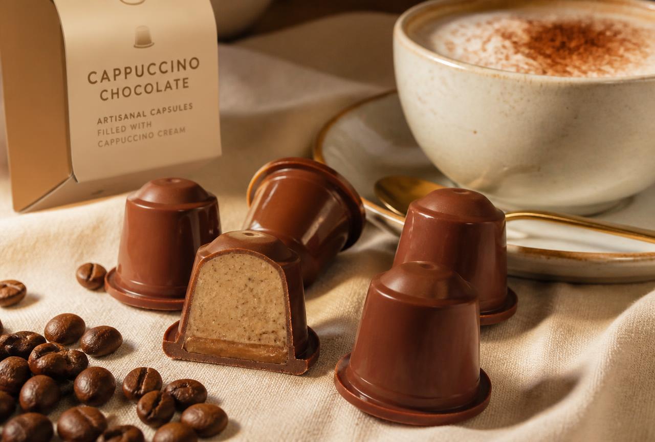 Cápsulas artesanais de cappuccino em chocolate ao lado de uma xícara cremosa